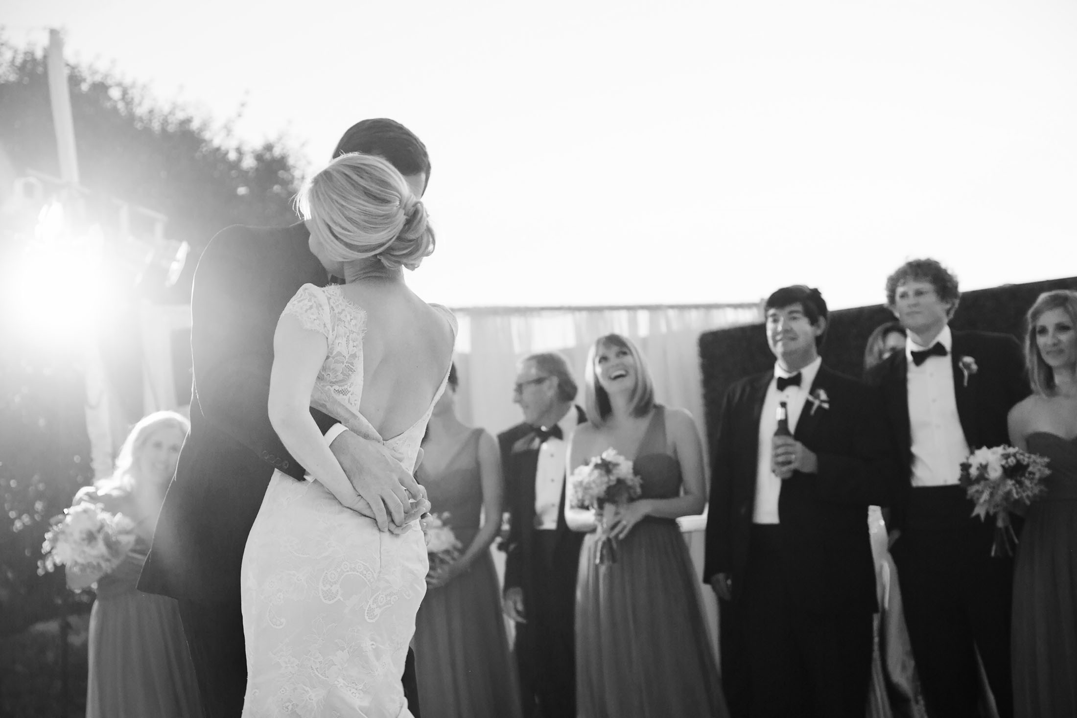 photo at a Rancho Valencia wedding by jennifer dery showing a reception on the croquet lawn. couple is dancing their 1st dance with bridal party in the background.